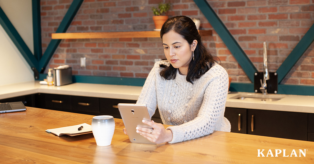 Woman seated at table conducting research on a tablet device.