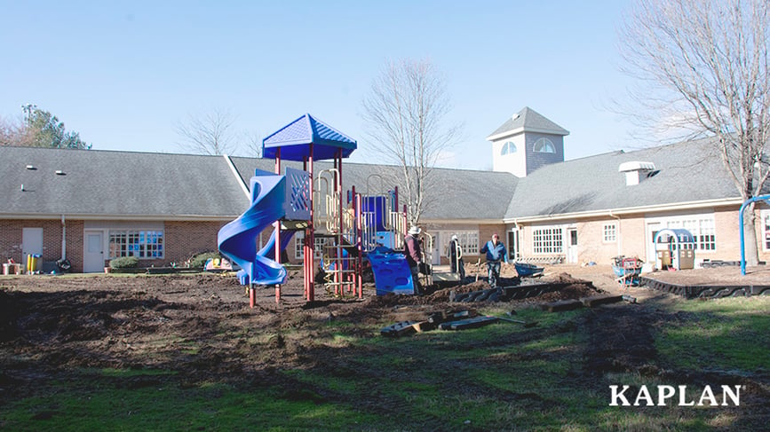 Playground installers rake piles of dirt around newly installed playground equipment. 