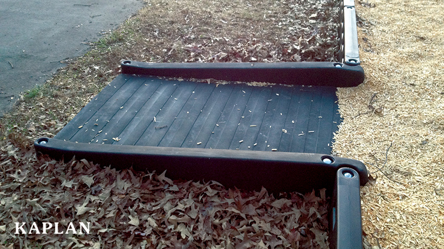A black rubber ADA/Wheelchair Accessible Ramp leading from a parking lot into a play area.