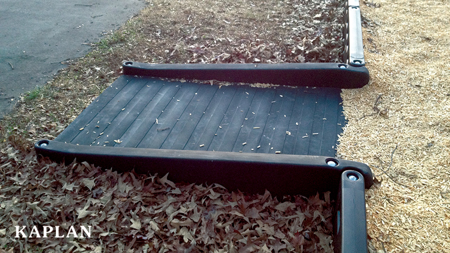 An up close image of a black, ADA/Wheelchair accessible ramp that leads into a playground with wood mulch surfacing.