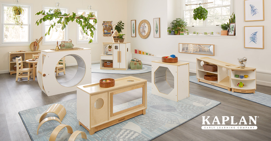 Toddler classroom filled with natural light, greenery, and a modular furniture system in white and birch.  Blue rugs anchor the furniture.