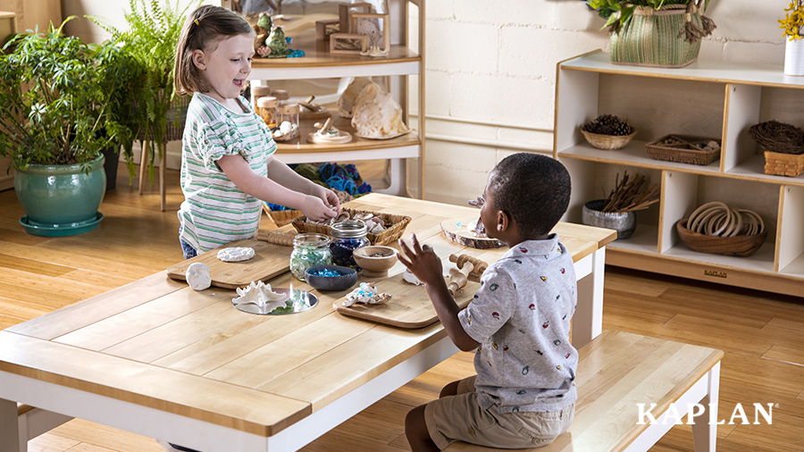  Two preschool students explore art and nature materials on a farmhouse table in a preschool classroom.