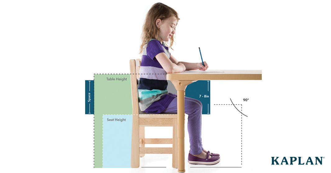 A young girl seated at a classroom table with her knees at a 90 degree angle, her feet lying flat on the floor, and the seat of the chair between 7 and 8 inches from the underside of the table.