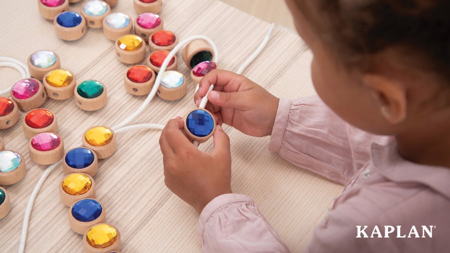 A child holds a string while placing it in the hole of a Wooden Lacing Jewel.