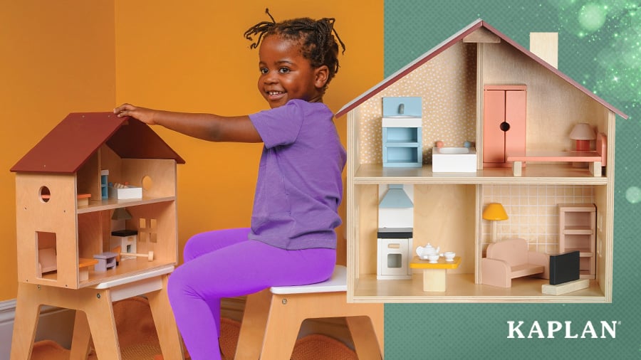 A child wearing purple clothing sits on a wooden stool while playing with a furnished Wooden Classic Dollhouse.