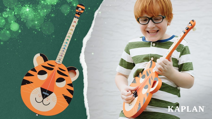 A child wearing glasses and a striped shirt smiles as he picks the strings on a TinkerTar Tiger Guitar. 