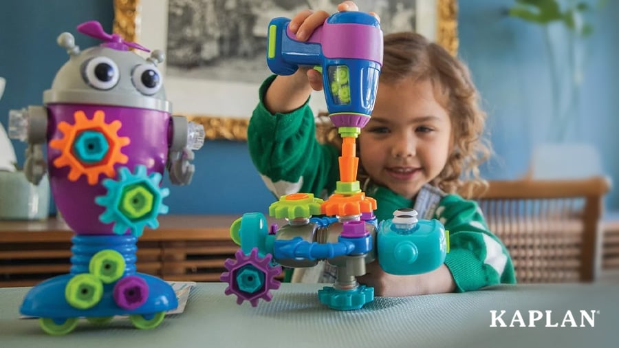 A child smiles while using a toy screwdriver to secure the bolts on a Design and Drill Robot. 
