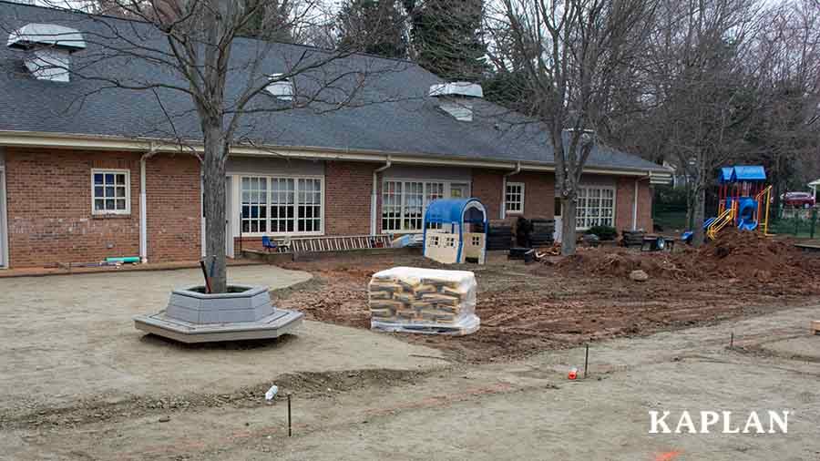 An image of the outside view of an early childhood facility in the process of renovating their playground by removing all of the grass, leaving a bare, muddy area behind. 