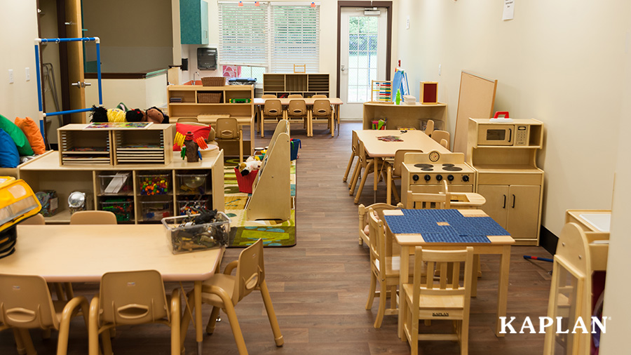An early childhood classroom is set up with newly assembled wooden shelving, tables and chairs, toys, a dramatic play area, a reading area, and an art center.