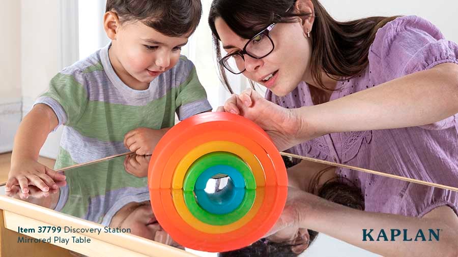 A young child and an early childhood teacher look at the Rainbow Arch blocks which are sitting on top of the Discovery Station Mirrored Play Table. 