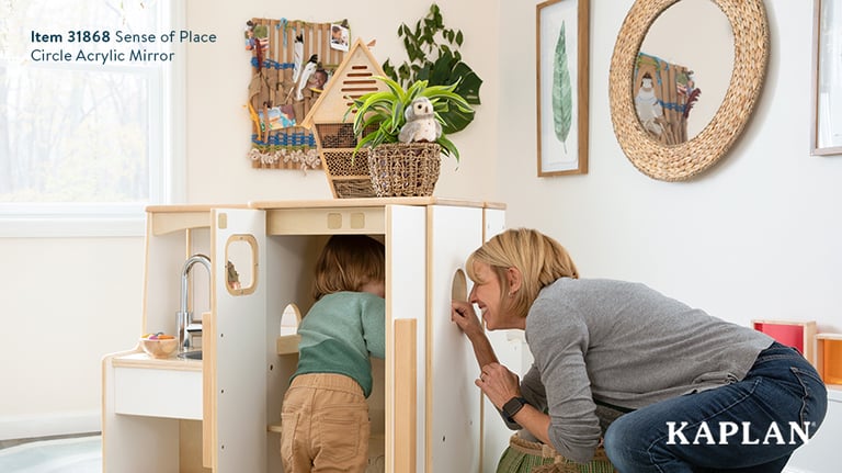 A teacher and young toddler play peek-a-boo through an open cutout in the Sense of Place Kitchen set. 