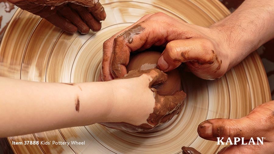An image of a child's hands and an adult's hands touching brown clay as it spins on the Kaplan Kids' Pottery Wheel. 