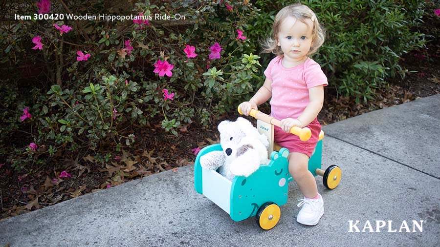 A young child in a pink shirt sits on the blue Wooden Hippopotamus Ride-On toy. 