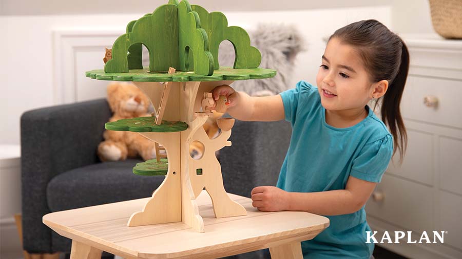 A young child places a wooden bird on a branch of the Woodland Trail Treehouse. 