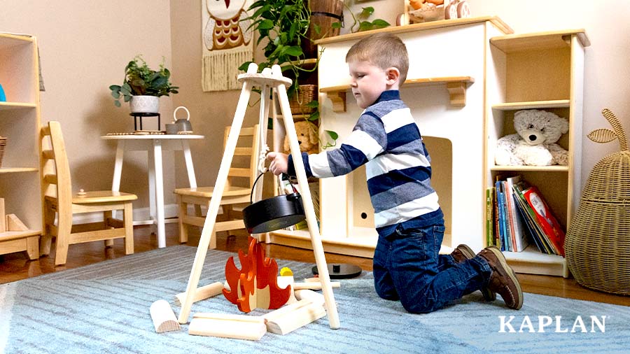 A young child places a black wooden pot over a pretend fire as he plays with the Home on the Range Camping Set. 