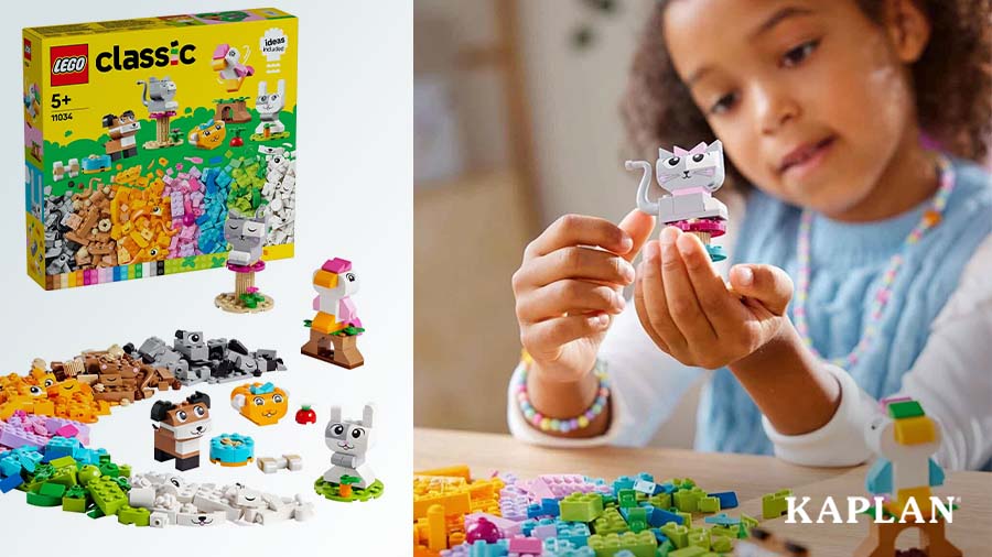 A young girl sits at a table with Lego pieces strewn about, in the child's hand is a LEGO cat made using gray LEGO bricks. 
