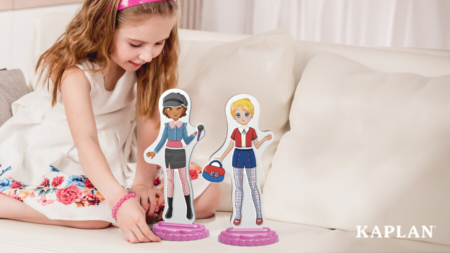 A young girl sits on a white couch, she is holding a Magnetic Fashion Doll Best Friend with one hand. 