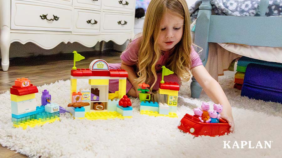 A young child is pushing a red car full of Peppa Pig figurines toward the LEGO DUPLO Peppa Pig Market.