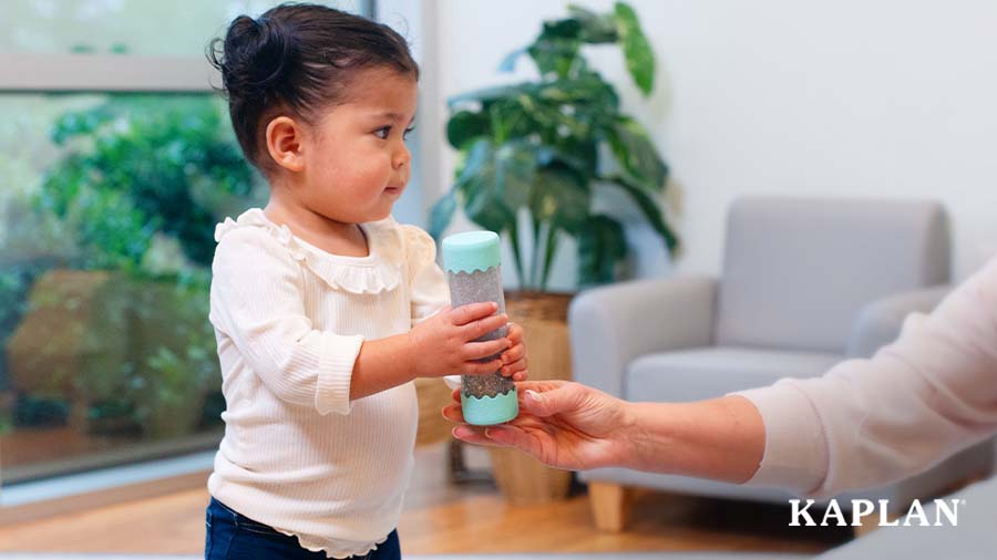 An adult is holding a Baby Calm Down Sensory Bottle, a young child is standing near the adult, grabbing the Sensory Bottle. 
