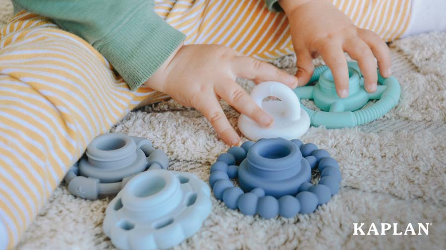 An image of an infants hands grasping pieces of a Rainbow Stacker Soothing Teether. 