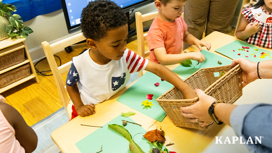 Young children sit around a wooden classroom table, they are working on the Nature's Symmetry activity that involves creating symmetrical images on a green sheet of construction paper.