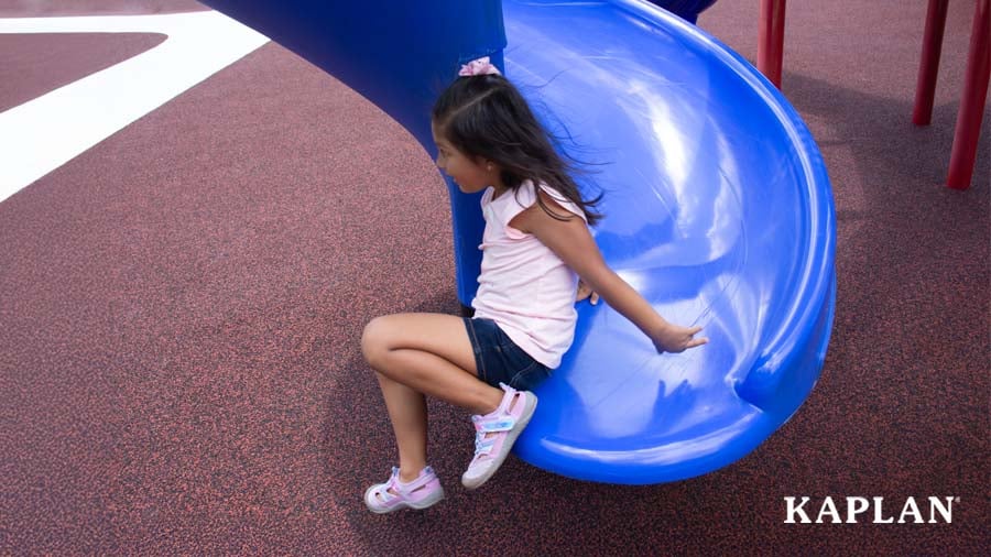 A young girl gets off a blue slide and steps onto a poured-in-place-rubber playground surface