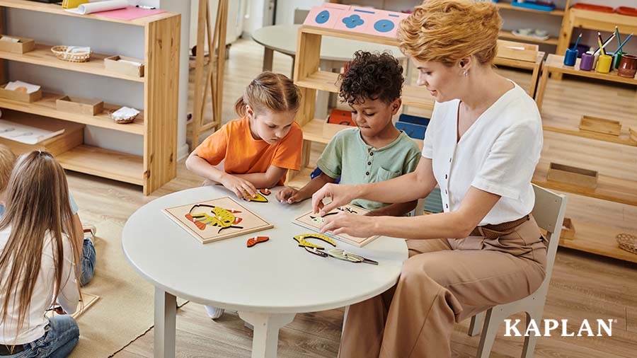 An early childhood teacher sits at a table with two children, the three of them are adding pieces to complete a wooden fish puzzle.