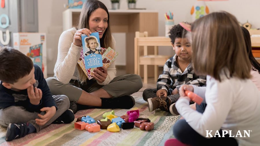 An early childhood teacher sits with a small group of children while holding up a flash card with emotions on it. 