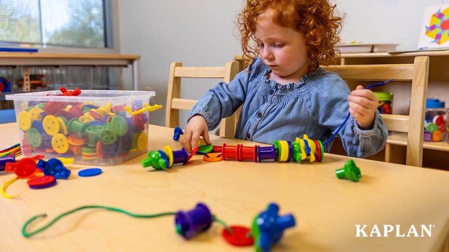 Child sitting at table lacing multicolored manipulatives on a string