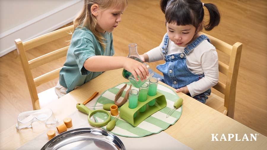 Two young children pour green liquid into test tubes during a hands-on science exploration activity