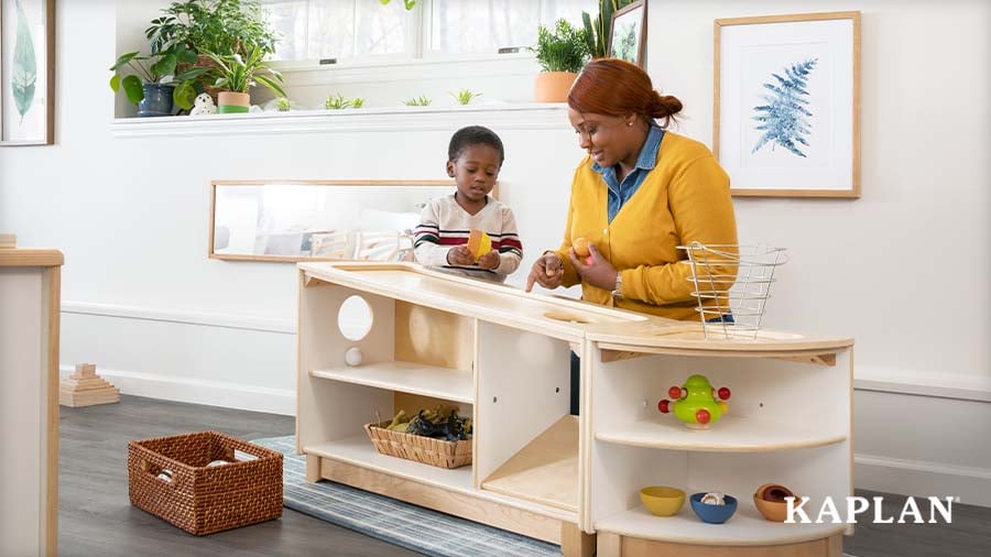 A family caregiver and young child explore sensory materials together at a wooden activity center