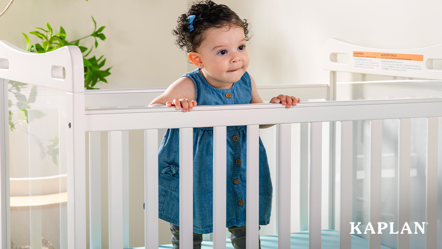 Infant standing up in a white crib with clear side panels