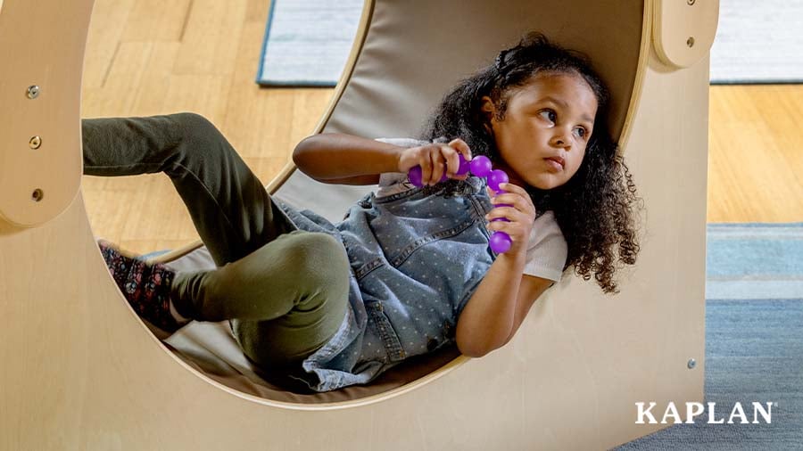 A young child sits inside the Carolina Connections Cove while holding a purple Bendi Bead in their hand.