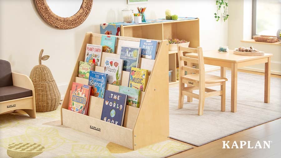 A Kaplan wooden bookshelf filled with children's books in a bright corner of an early childhood classroom