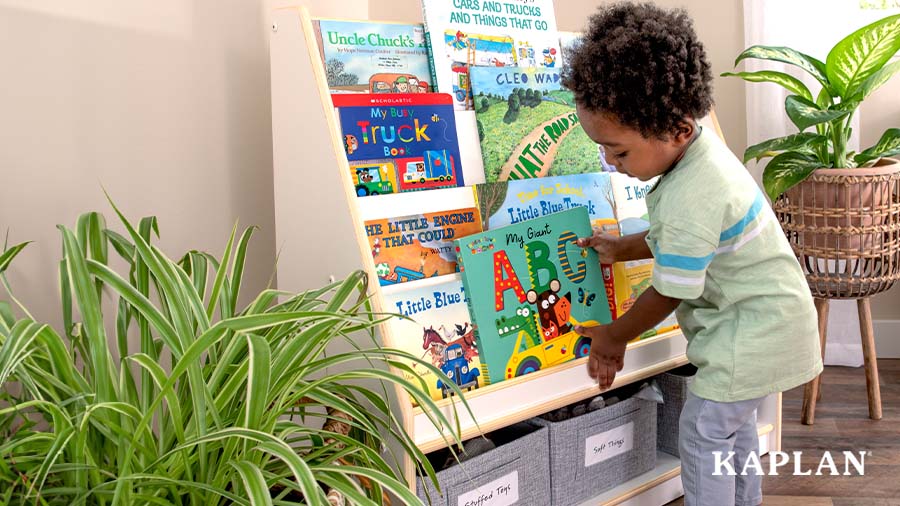 A young child in a green shirt places the book My Giant ABC's on a classroom bookshelf. 