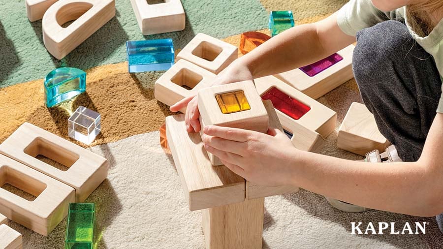 Child building structures with wooden blocks and multicolored prisms
