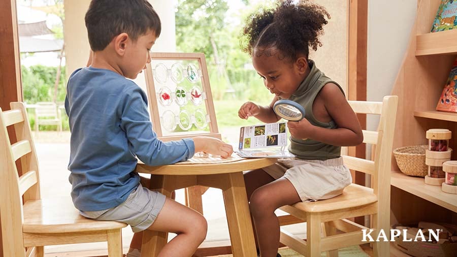 A preschool-aged boy and a preschool-aged girl sit at a round wooden table and examine nature-inspired acrylic stones