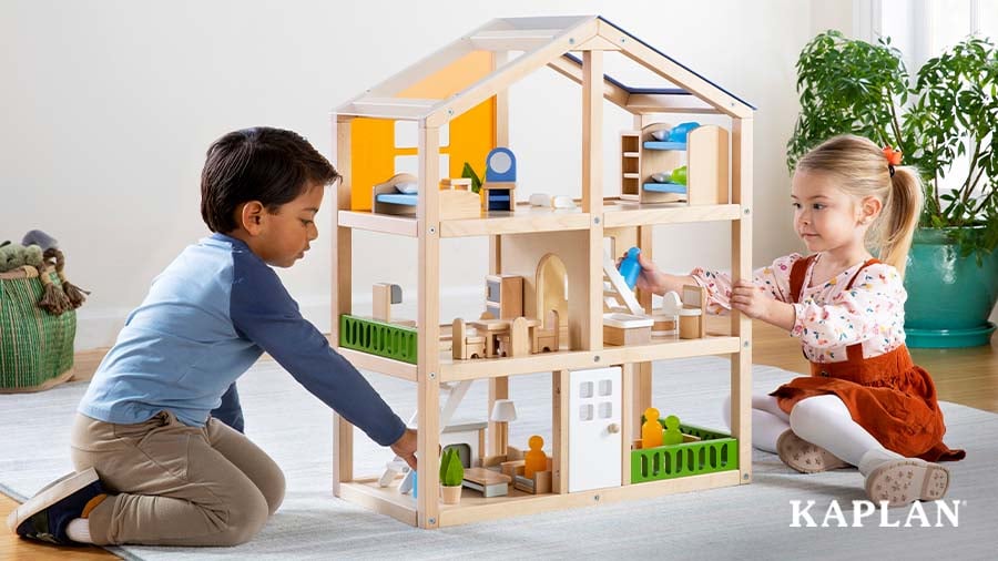 A preschool-aged boy and a preschool-aged girl play with miniature figurines on different levels of a multilevel dollhouse