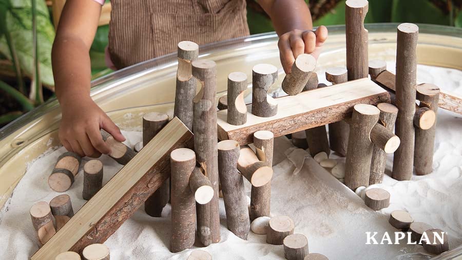 Child building wood structures in a sand table