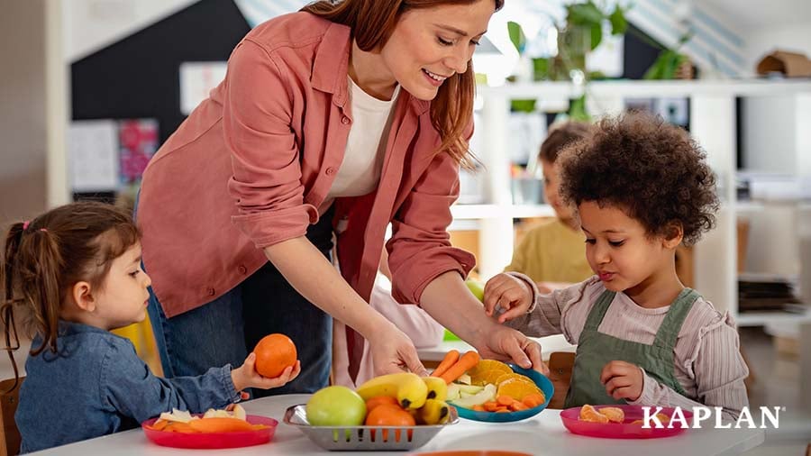 Early childhood educator serving two children fruit during snack time