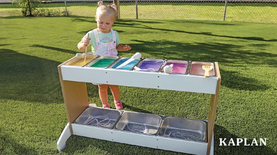 Young child paints at an outdoor sensory table with multiple paint colors