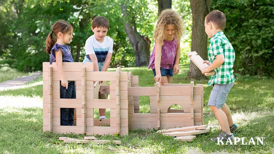 Four young children building a tall structure with large outdoor blocks