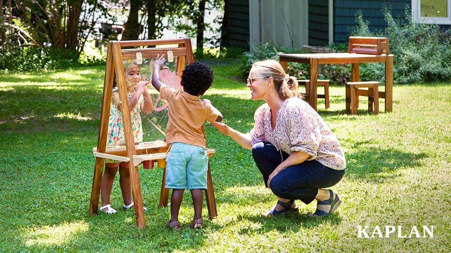 Early childhood educator and two young children use a double-sided art easel for an outdoor painting activity