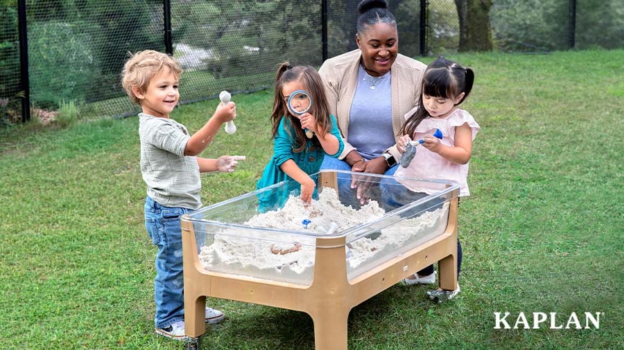 Early childhood educator and three young children digging for pretend fossils in an outdoor sand and water sensory table