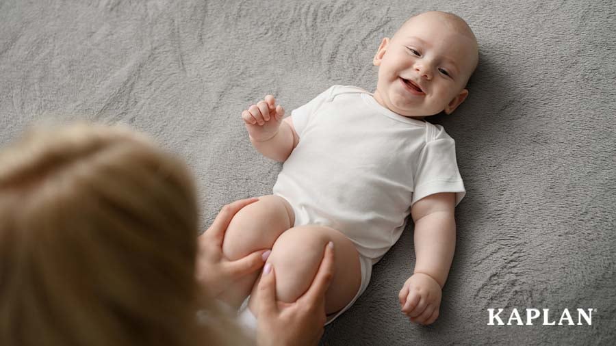 Infant lying on carpet while early childhood educator moves their legs