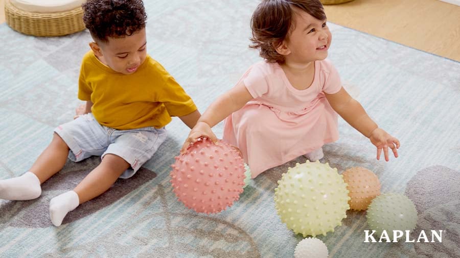 Two infants playing with sensory balls on the carpet