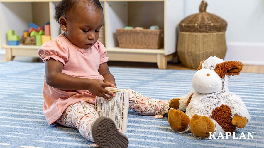 Toddler on the carpet with a book in hand and plush animal in view