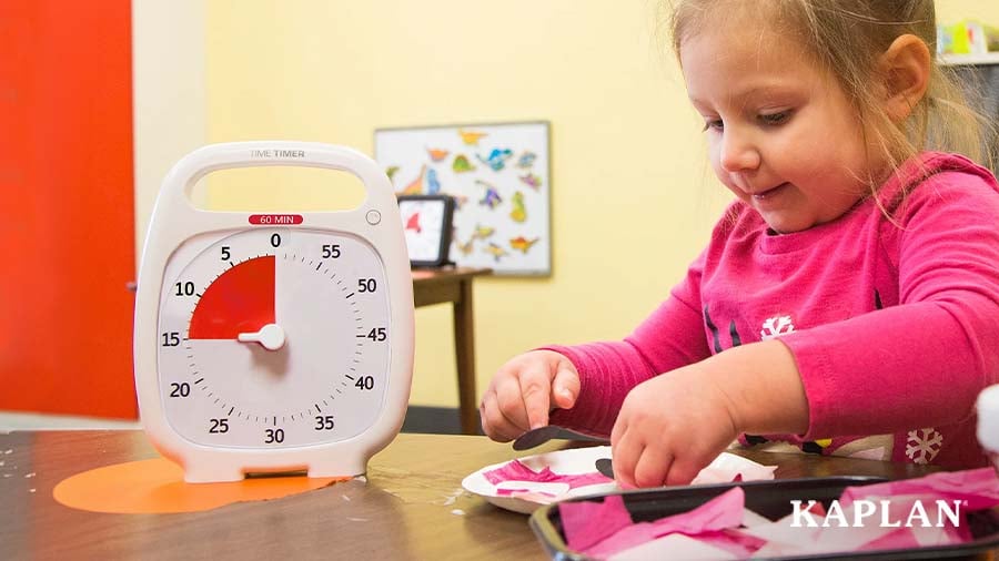Toddler sitting at a table working on a craft with a timer in view
