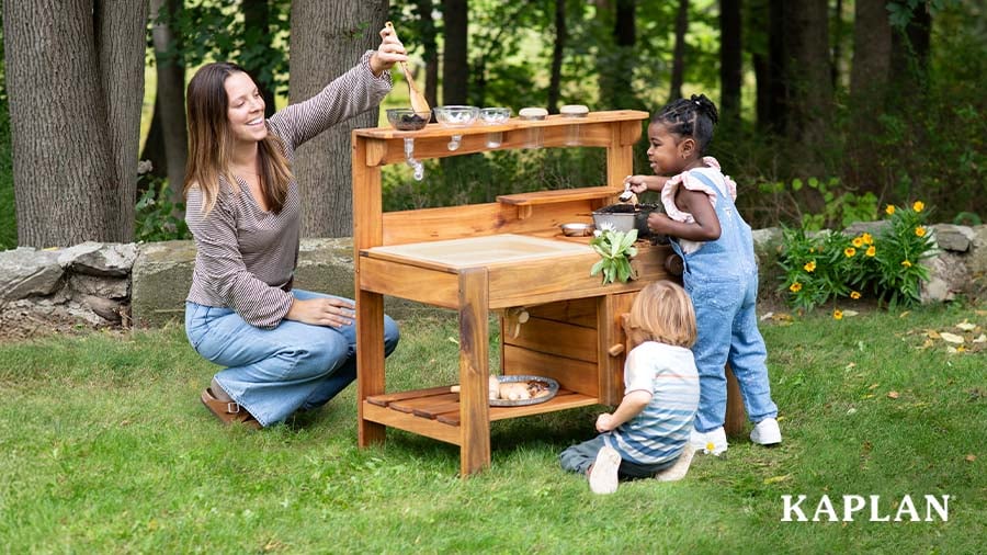 Two children playing at an outdoor mud kitchen with an early childhood educator