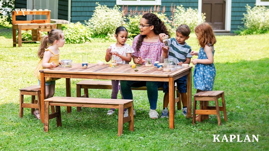 Early childhood educator with children using wood outdoor furniture to learn and explore